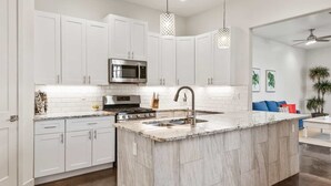 A modern kitchen with white cabinetry, a stainless steel stove, and a large island with a sink. - Highlander: Private Hot Tub, Sleeps 21, pool+pickleball courts, Foosball (Hurricane)