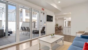 A spacious living area with a sliding glass door leading to an outdoor patio, a dining area, and a kitchen. - Highlander: Private Hot Tub, Sleeps 21, pool+pickleball courts, Foosball (Hurricane)