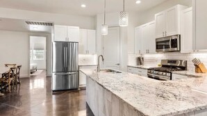 A modern kitchen with white cabinets, stainless steel appliances, and a marble island. - Highlander: Private Hot Tub, Sleeps 21, pool+pickleball courts, Foosball (Hurricane)