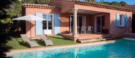 A house with a swimming pool, a patio with chairs, and a covered outdoor area.