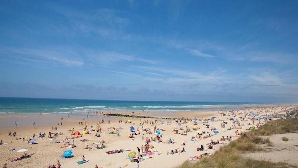 Ein weiter Sandstrand mit Menschen, die sich sonnen und am Ufer entlangspazieren.