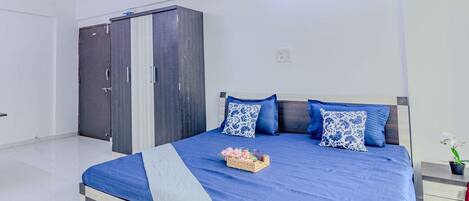 A bedroom with a large bed, a wardrobe, and a nightstand with a plant.