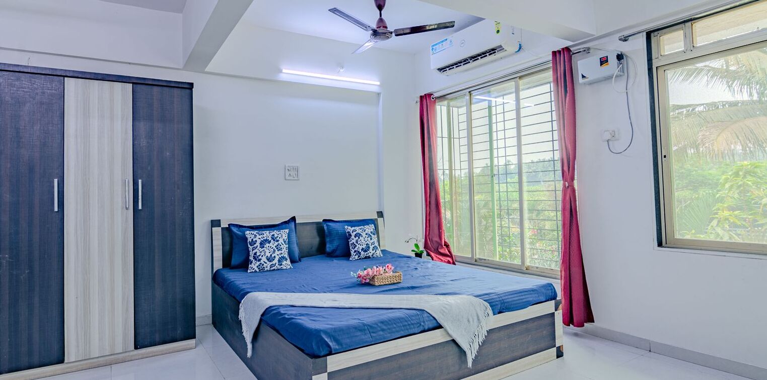 A bedroom with a bed, a wardrobe, a ceiling fan, an air conditioning unit, and a window with curtains.
