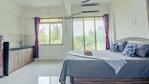 Une chambre à coucher avec un lit, une table de chevet, une fenêtre avec des rideaux et une vue sur la verdure à l’extérieur.