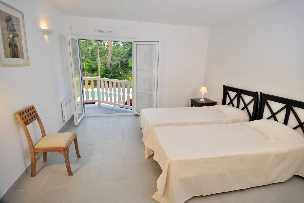 Une chambre avec deux lits, une chaise, une table de chevet et un balcon doté d’une balustrade.