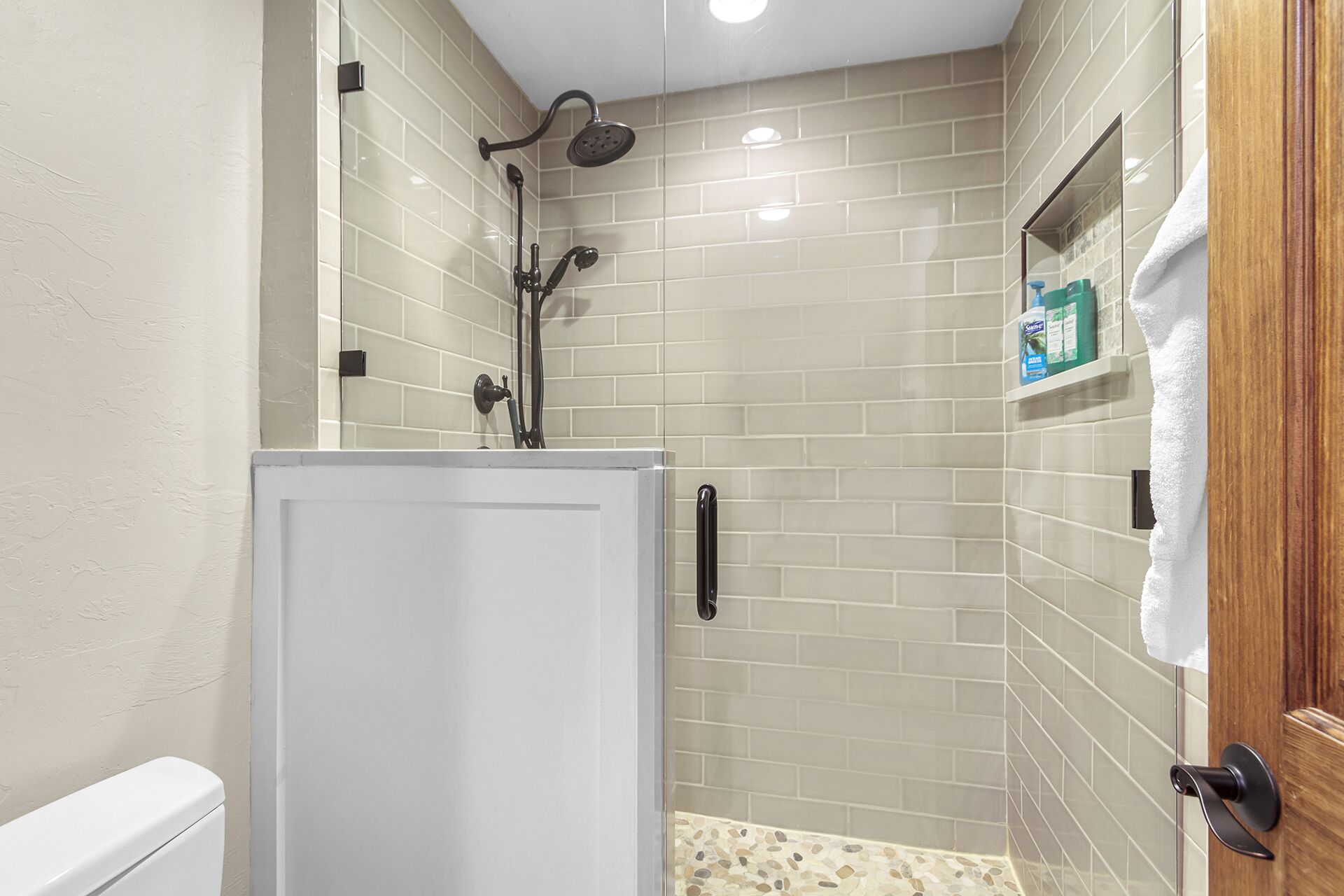 A shower area with a glass door, tiled walls, and a small shelf with toiletries.