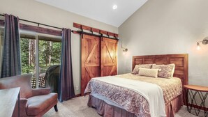 Un dormitorio con una cama grande, una silla, una mesita pequeña y una puerta corrediza de estilo rústico.