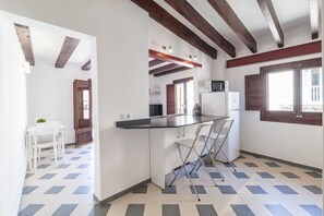 A kitchen with a white countertop, bar stools, and a microwave. There is a dining table with chairs in the adjacent room. - Can Boss Turismo de Interior  (Palma de Mallorca)
