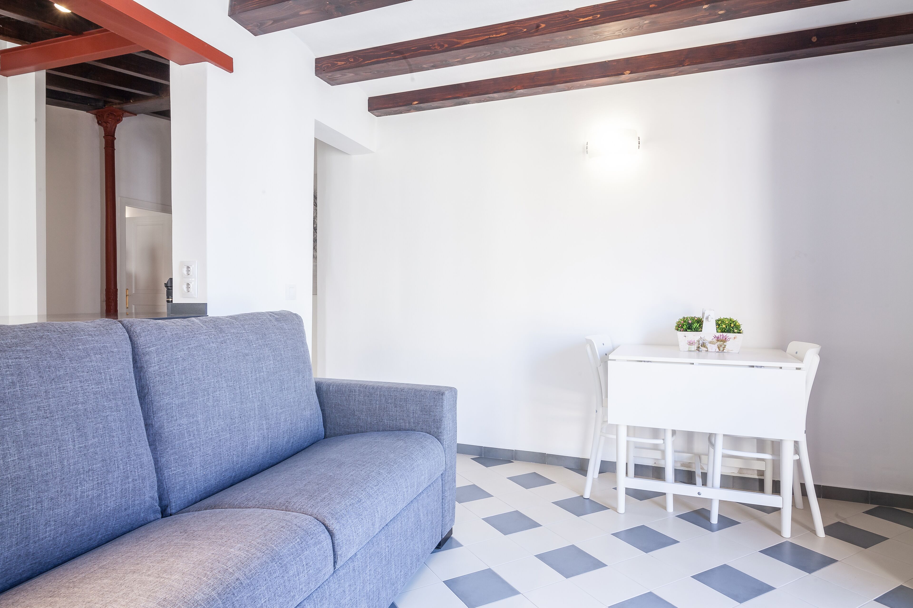 A room with a grey sofa, a white table with two potted plants, and a checkered floor.