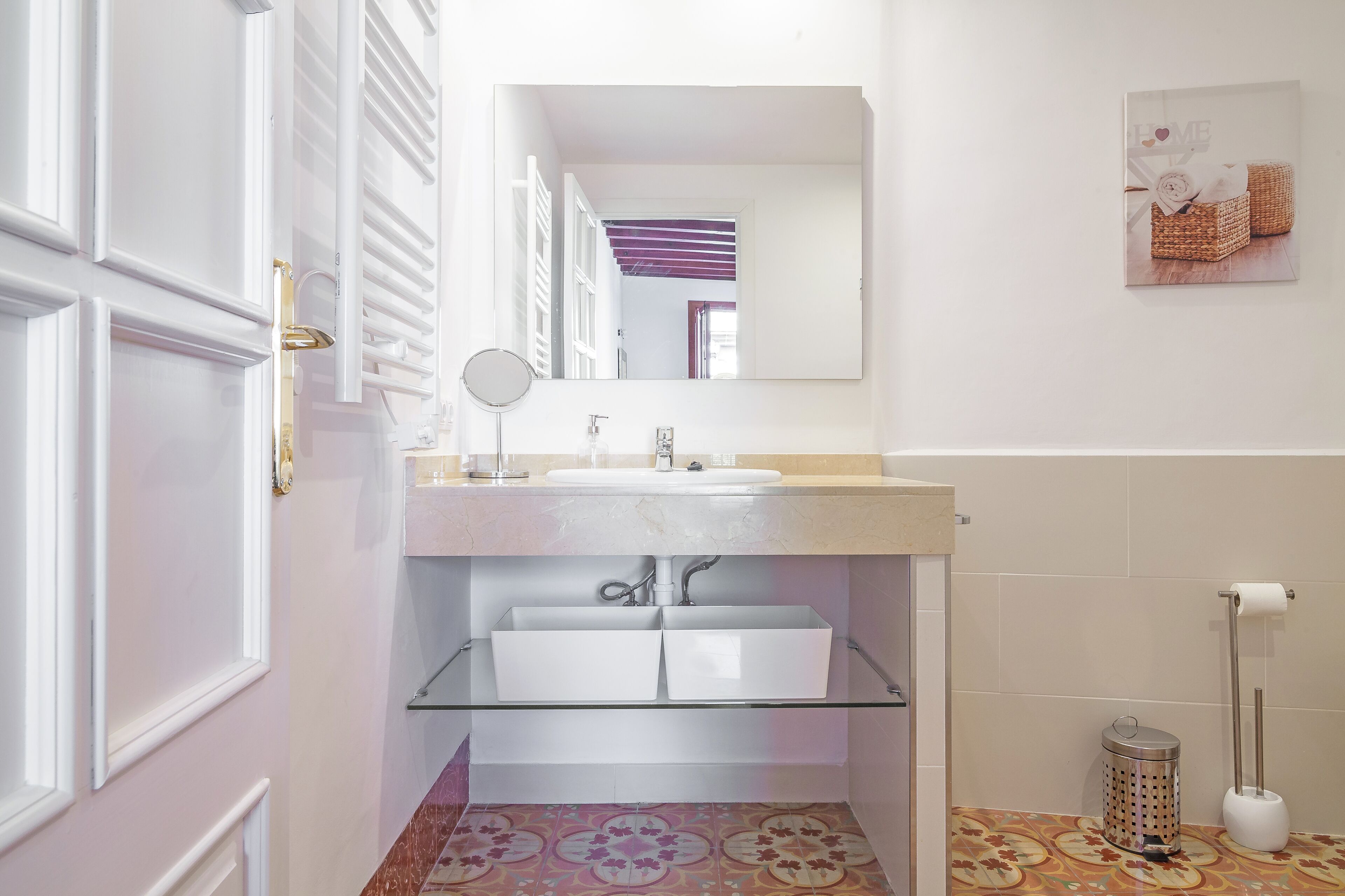 Un baño moderno con un estante de vidrio debajo del lavabo, un dispensador de papel higiénico blanco y un piso con diseño.