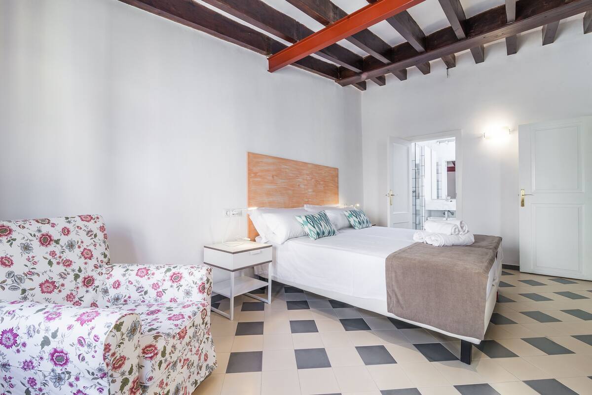 Un dormitorio con cama, mesita de noche y una silla con estampado floral.