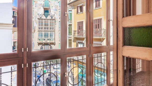 Vista a través de una ventana de madera con múltiples cristales, que da a una calle con edificios de colores y una fuente.