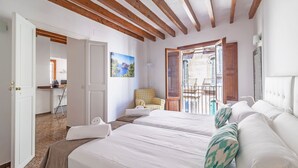 Habitación de hotel con dos camas, un balcón con vistas y un comedor visible a través de una puerta abierta.