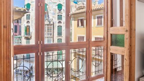 Vista a través de una ventana de madera con múltiples divisiones, mostrando una calle con edificios y balcones coloridos.