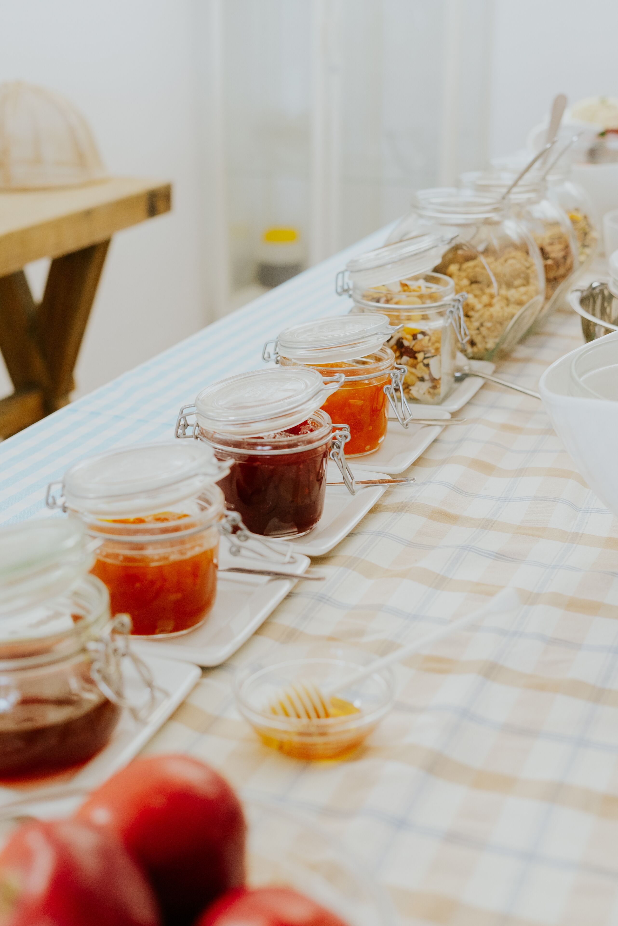 A buffet table with various food items in glass containers, a wooden table, and a checkered tablecloth.