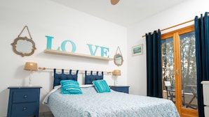 A bedroom with a bed, two nightstands, a wooden headboard, a 'LOVE' sign, a mirror, and a view through a glass door. - Xenios Zeus Hotel  (Sithonia)