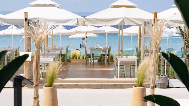 An outdoor dining area with white umbrellas and tables, overlooking a body of water. - Xenios Zeus Hotel  (Sithonia)