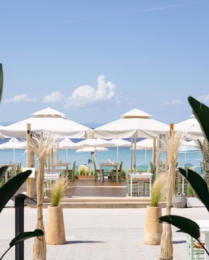 An outdoor dining area with white umbrellas and tables, overlooking a body of water. - Xenios Zeus Hotel  (Sithonia)