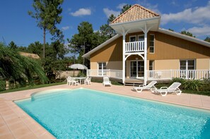 A two-story house with a swimming pool, outdoor furniture, and a covered patio area.