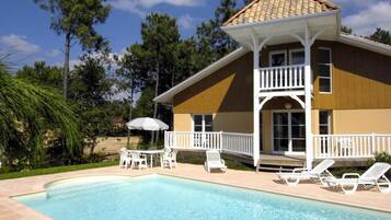 Une maison à deux étages avec une piscine, des rampes blanches et du mobilier d’extérieur.