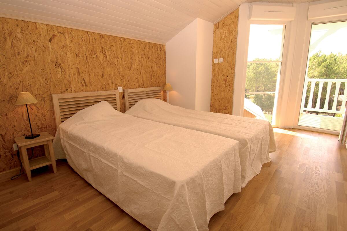 Ein Schlafzimmer mit zwei Betten, Holzboden und einem Balkon mit Geländer.