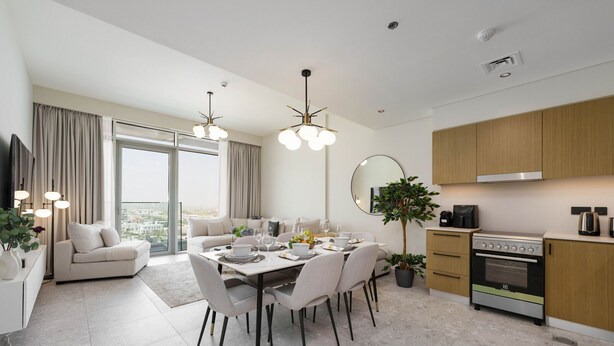 A modern living room with a dining area, a large window, and a kitchen with wooden cabinets and a stove.