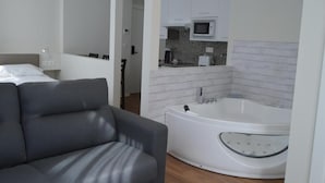 Una habitación de hotel moderna con un sofá gris, una bañera blanca y una kitchenette con microondas.