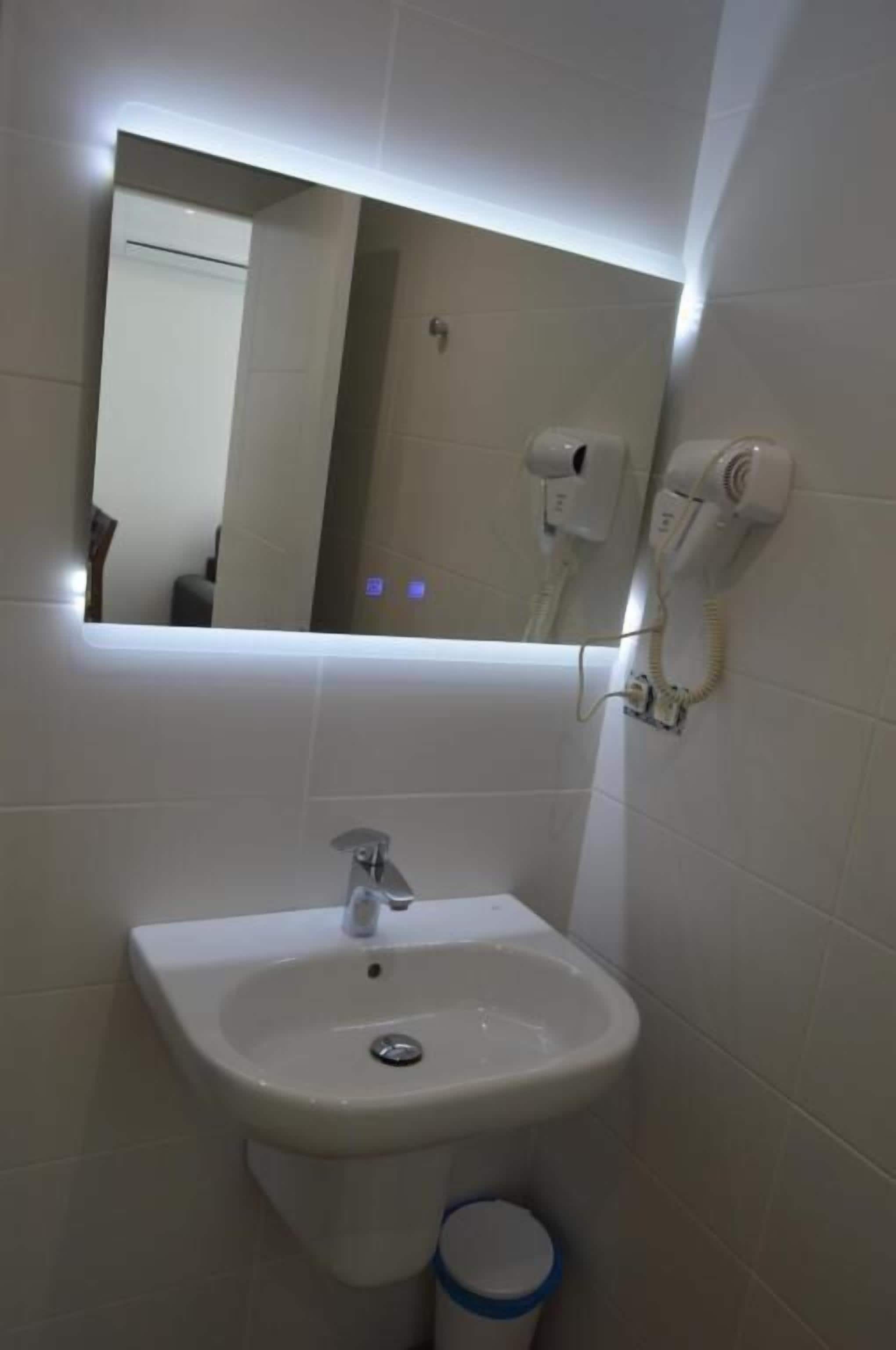 Un baño con un lavamanos blanco, un espejo y un secador de pelo montado en la pared.