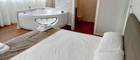 Una camera d'albergo con un letto, una vasca da bagno bianca e un pavimento in legno.
