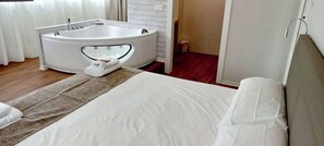 A hotel room with a bed, a white bath tub, and a wooden floor. - Apartamentos el Beyu (Cangas de Onis)