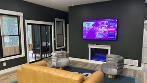 A modern living room with a large flat-screen TV mounted on the wall, a fireplace, and a sofa. - Luxurious Speakeasy Lodge, Hot Tub, Wifi & Hidden Speakeasy! Mins from the Caves (Logan)