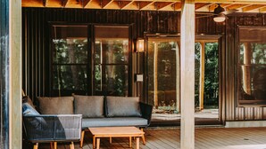 A wooden deck with a sofa and chairs, large windows, and a ceiling fan. - Luxurious Speakeasy Lodge, Hot Tub, Wifi & Hidden Speakeasy! Mins from the Caves (Logan)