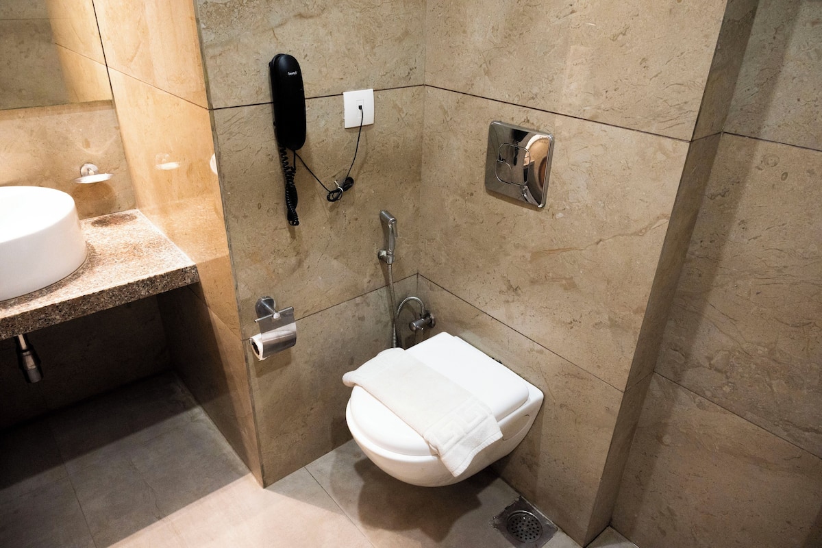 A bathroom with a white sink, a toilet, a hand dryer, and a telephone mounted on the wall.