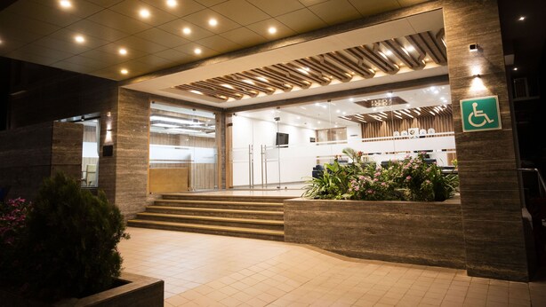 A hotel entrance with a ramp, a wheelchair accessibility sign, and a reception area with a modern design. - RAAJ SVASTIK INN (Jamnagar)