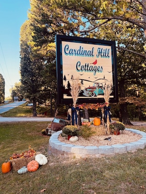A sign for Cardinal Hill Cottages with a rustic design, surrounded by autumn decorations and a vintage car illustration.