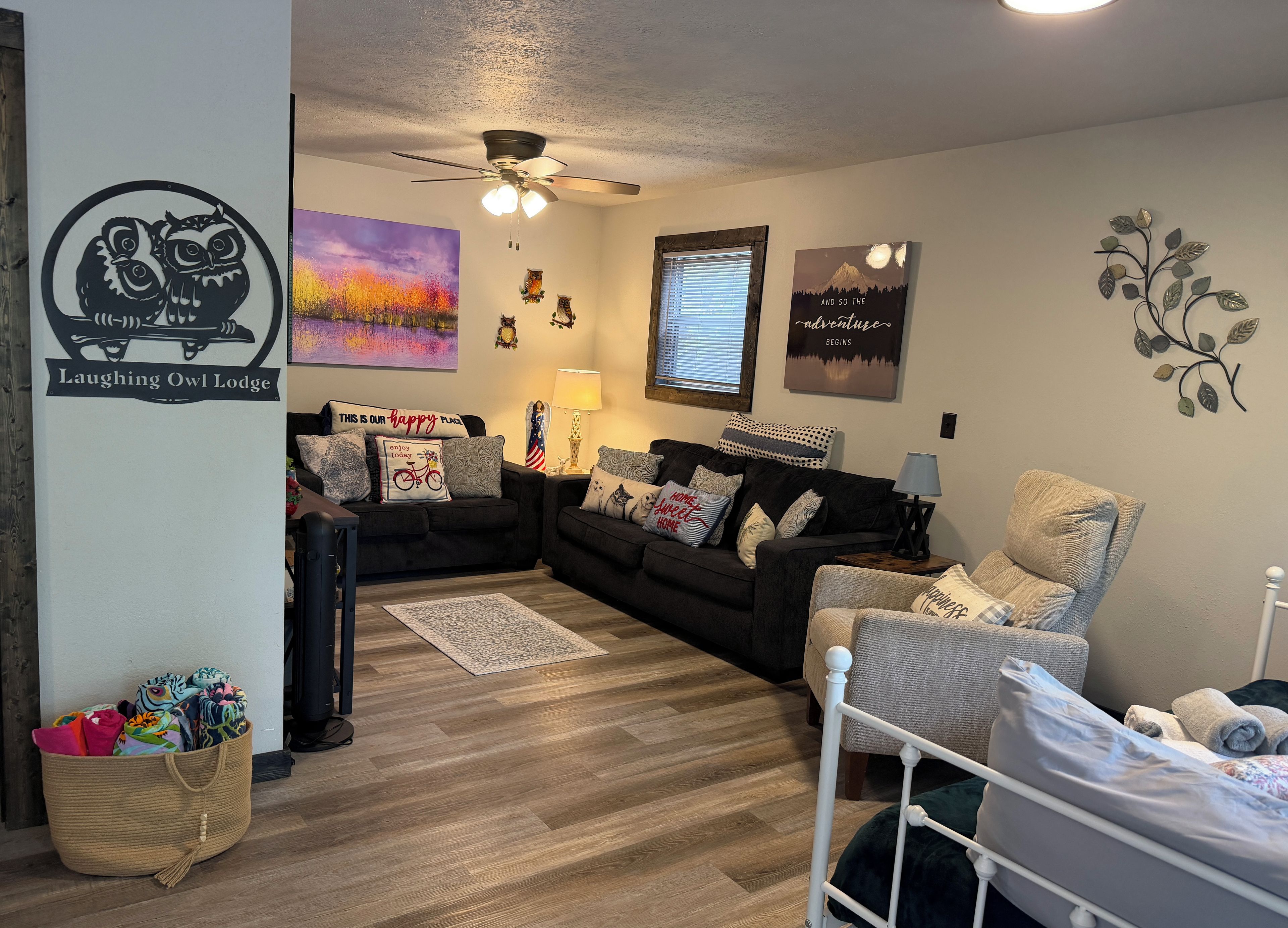 Un salon chaleureux avec un canapé aux couleurs foncées, un fauteuil aux couleurs claires, une petite table avec une lampe et un élément décoratif fixé au mur.