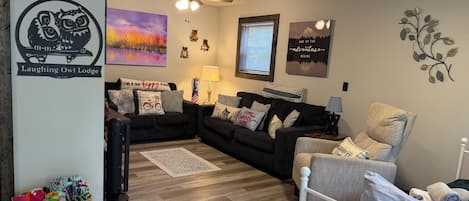 Un salon chaleureux avec un canapé aux couleurs foncées, un fauteuil aux couleurs claires, une petite table avec une lampe et un élément décoratif fixé au mur.