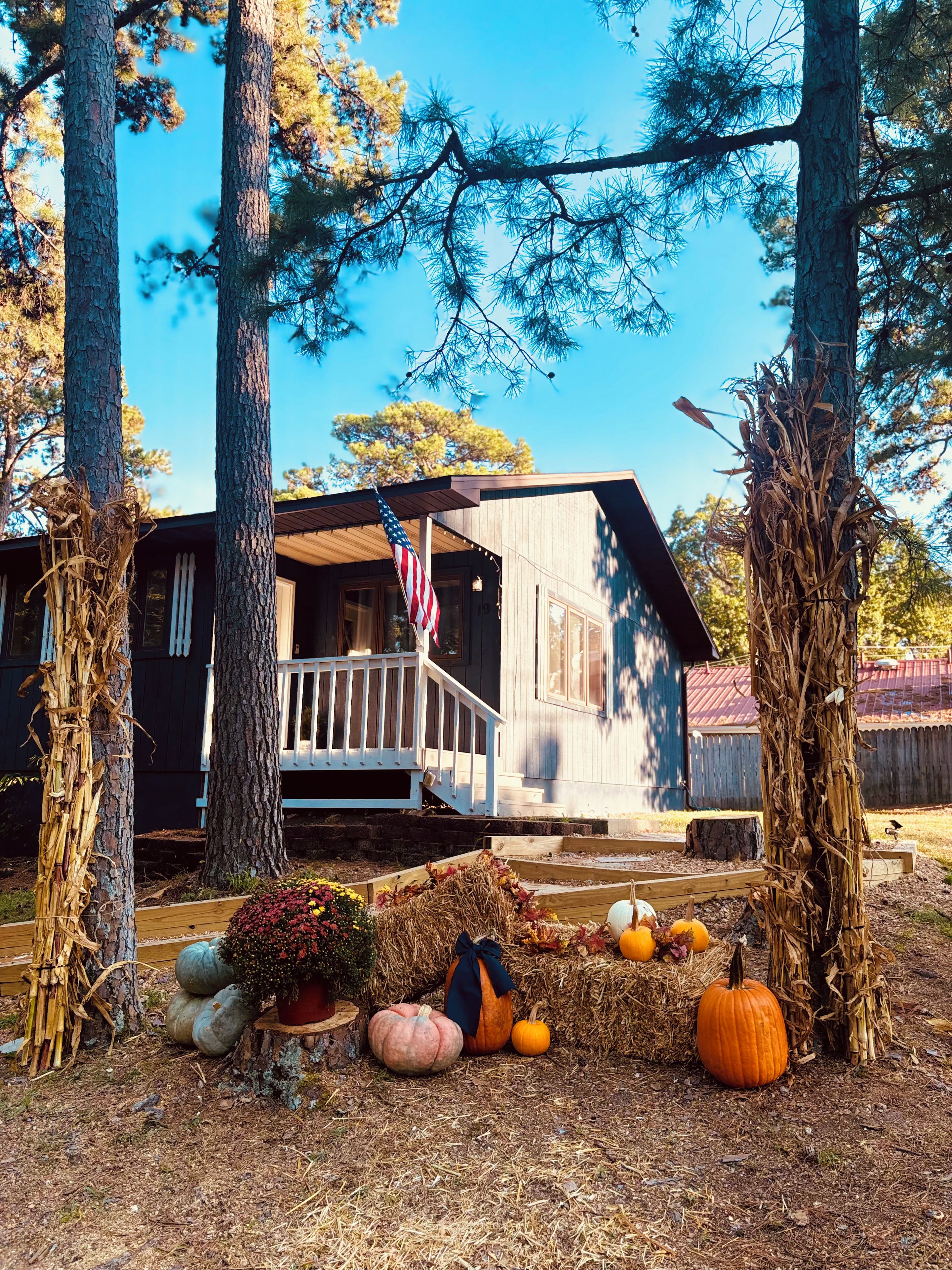 A rustic cabin with a porch, surrounded by trees and autumn decorations.