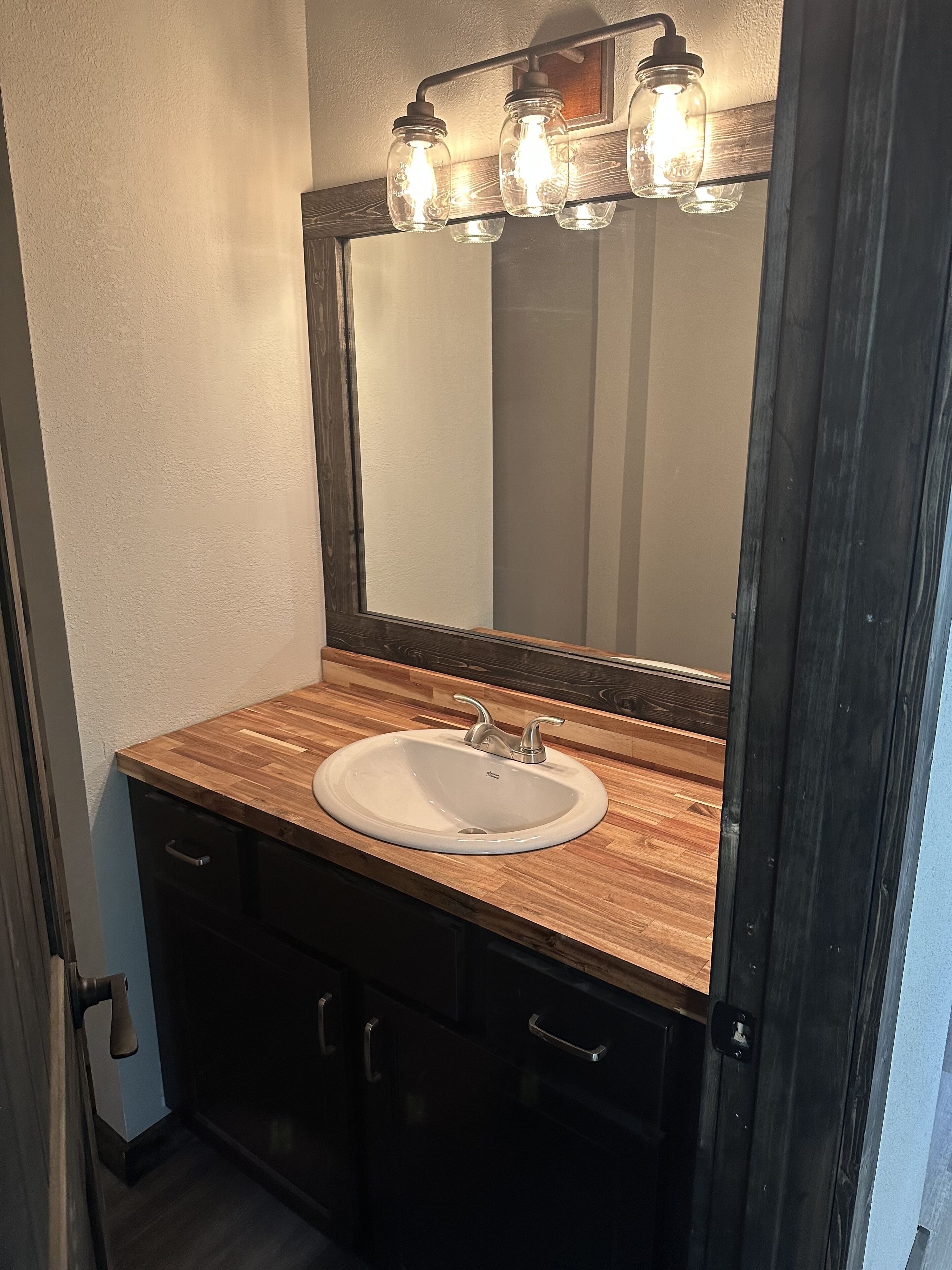 A bathroom with a wooden vanity, a white sink, and a mirror with a light fixture above it.