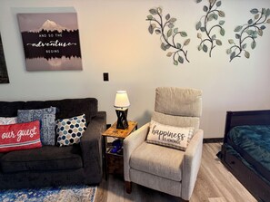 A cozy living room with a couch, armchair, and a wall-mounted lamp. - Little Owl Cabin #10 - Sleeps 6. Resort Pool&Spa, Fire Pit. SDC 1 mi. Dogs ok! (Branson)