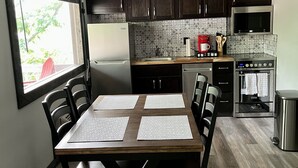 Una cocina moderna con armarios de madera oscura, un refrigerador de acero inoxidable, un microondas y un horno. Hay una mesa de comedor con cuatro sillas y dos individuales.