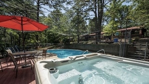 Un jacuzzi rodeado por una terraza de madera con sillas y un paraguas rojo.
