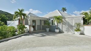 A modern house with a covered driveway, large potted plants, and a white fence.