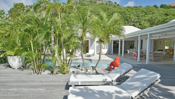 A poolside area with lounge chairs, a red horse statue, and lush greenery.