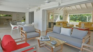 A spacious living area with a sofa, chairs, and a coffee table. There is a dining area with a table and chairs visible in the background.