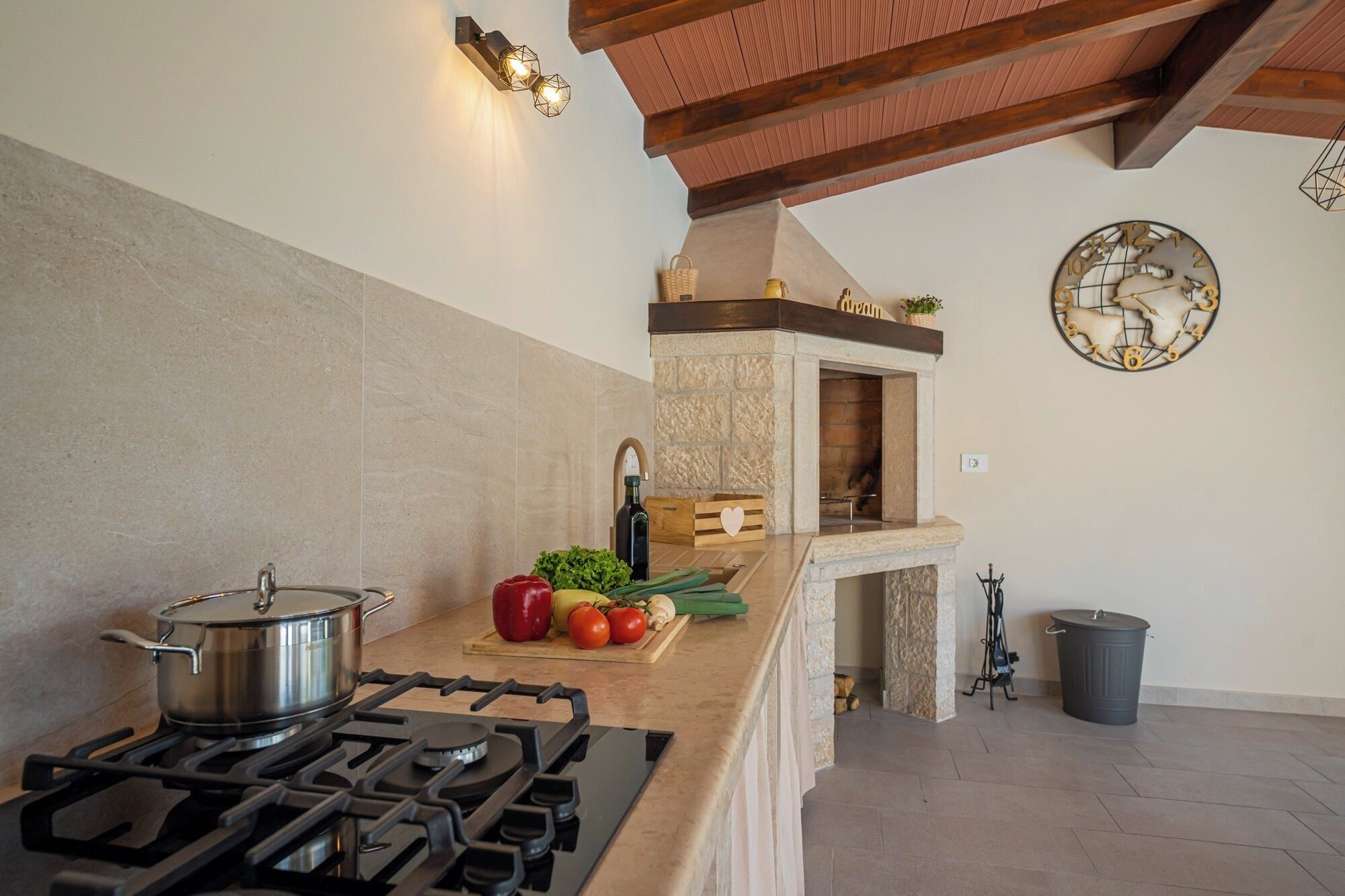 Een keuken met een gasfornuis, een stenen muur, een houten plafond en een wandklok.