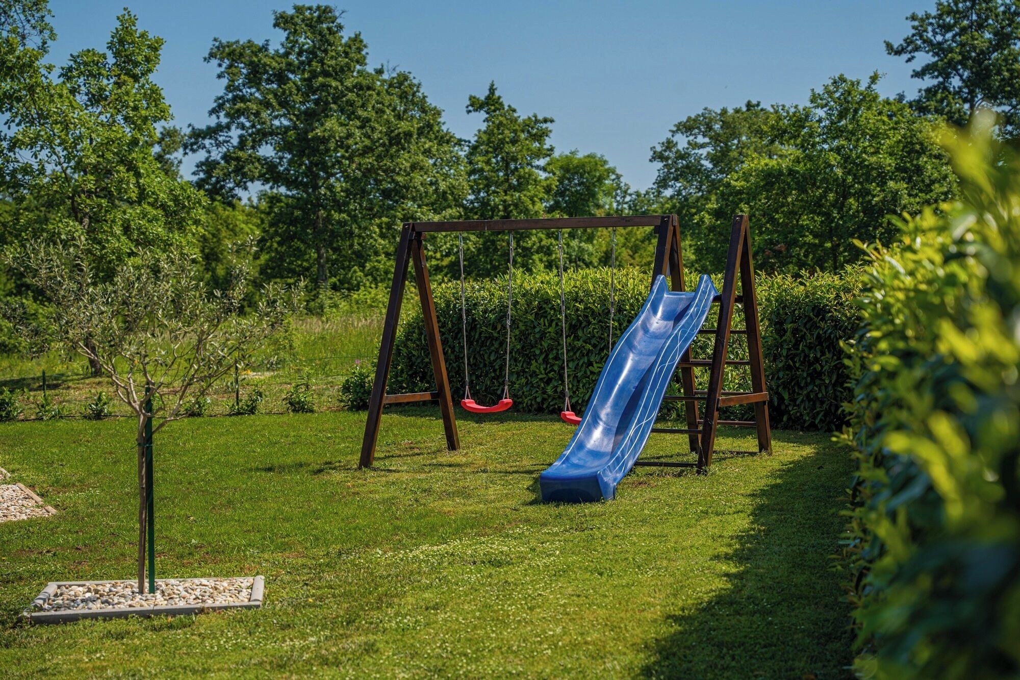 Un parque infantil con tobogán y columpios en un césped arbolado.