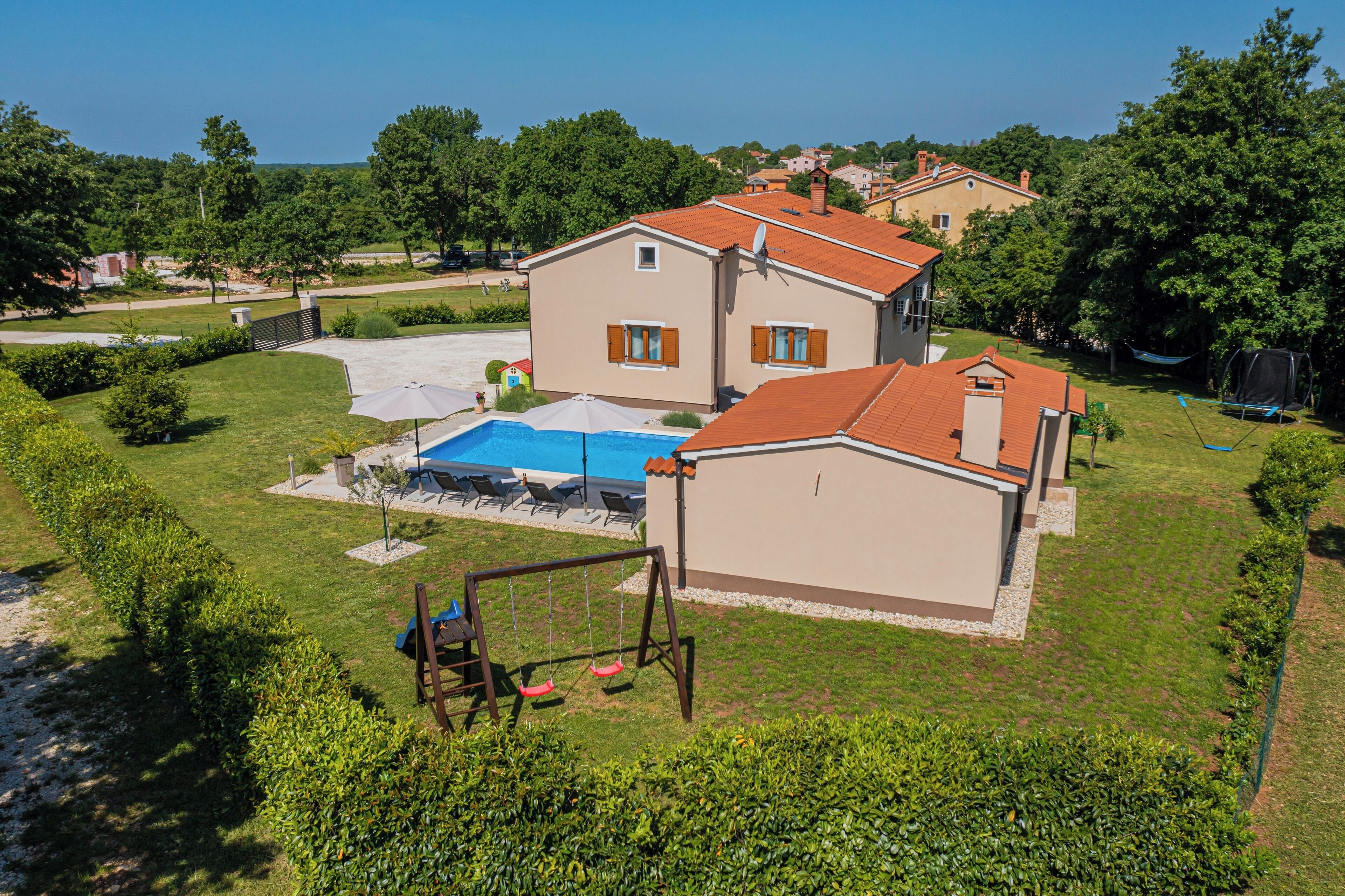 Uma casa de dois andares com piscina, balanço e quadra de tênis.