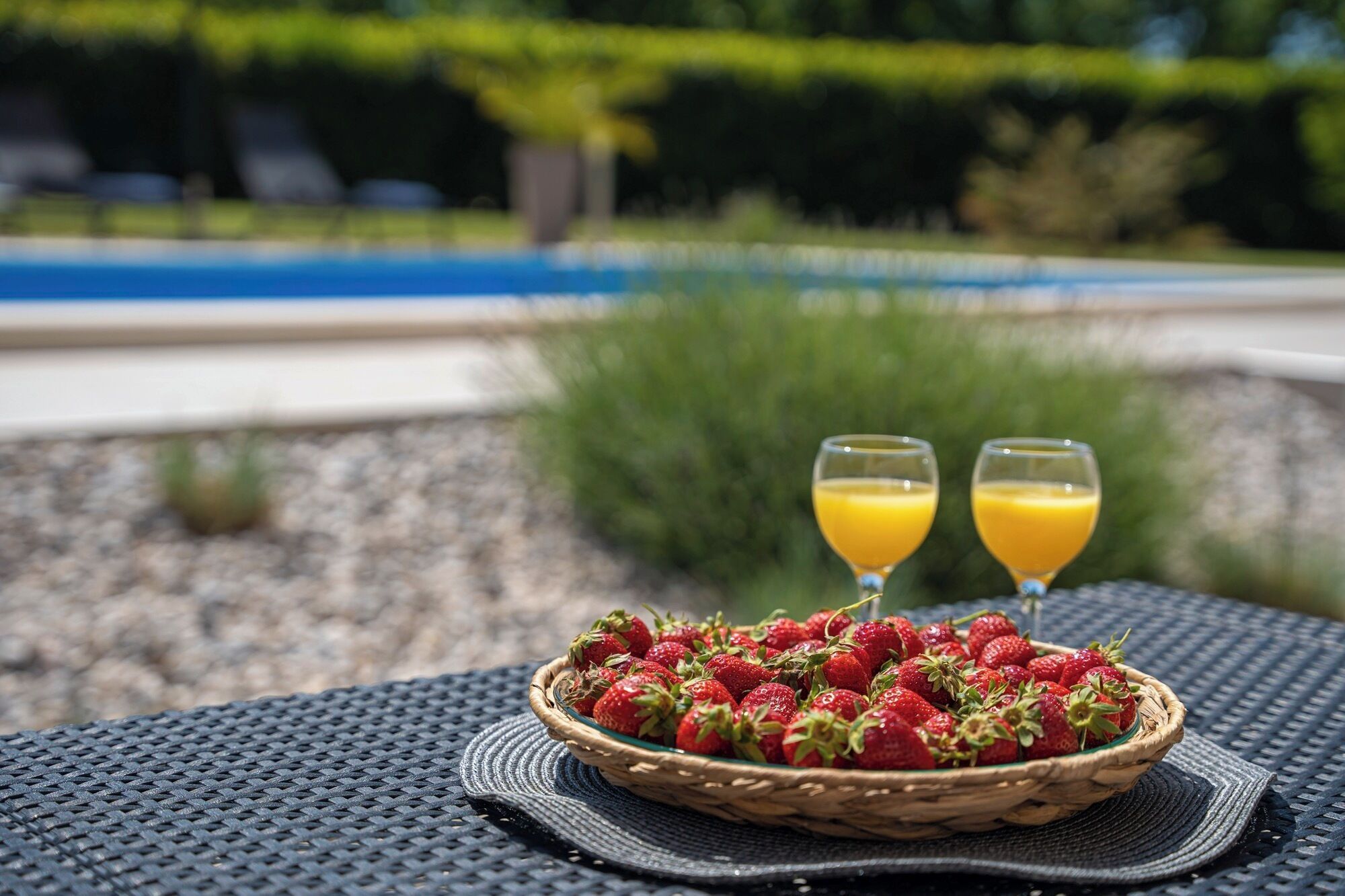 A wicker basket filled with strawberries on a textured tablecloth, with two glasses of orange juice in the background.