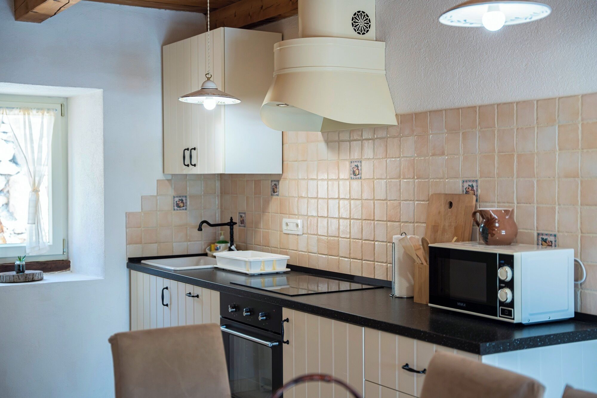 A kitchen with white cabinets, a black countertop, a microwave, and a window with curtains.